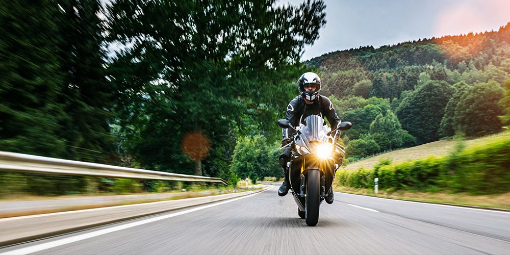 Motorcycle rider in black gear speeding on a winding country road - https://www.rogersvilleins.com/